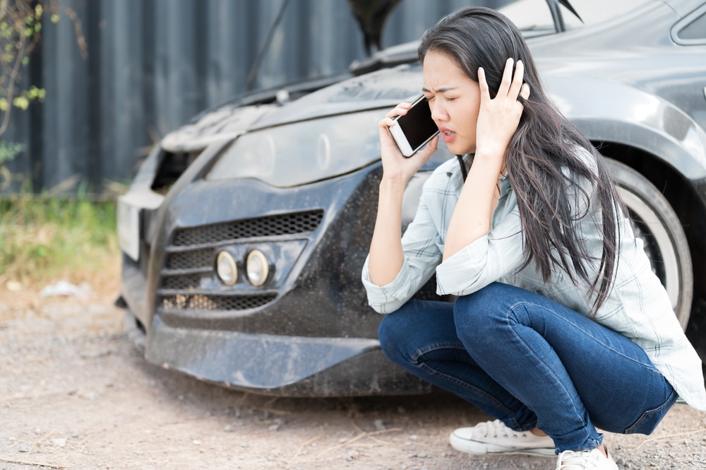 Car Accident Lawyer - Woman talking on a cellphone while sitting next to a broken down car